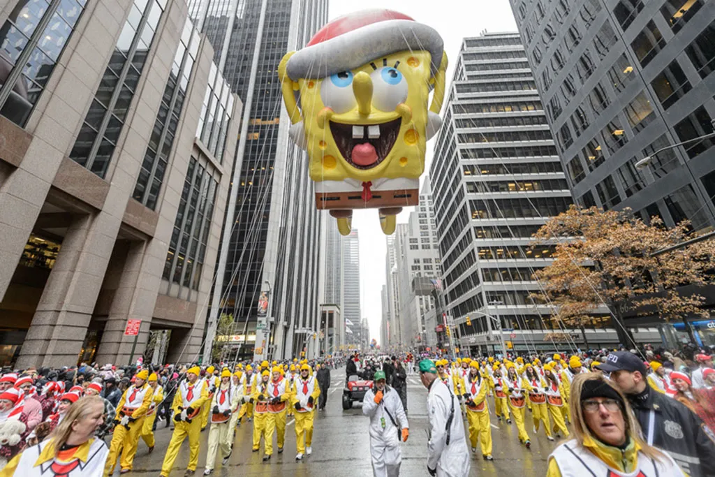 Cena vibrante do Desfile do Dia de Ação de Graças da Macy's, com balões gigantes, carros alegóricos coloridos e artistas performando em Nova York, atraindo milhões de espectadores todos os anos. Ideal para conteúdos sobre eventos icônicos e turismo nos Estados Unidos