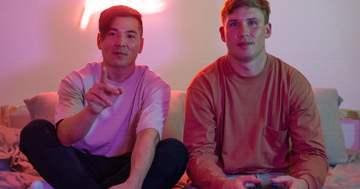 Dois amigos jogando videogame num quarto com luz neon rosa