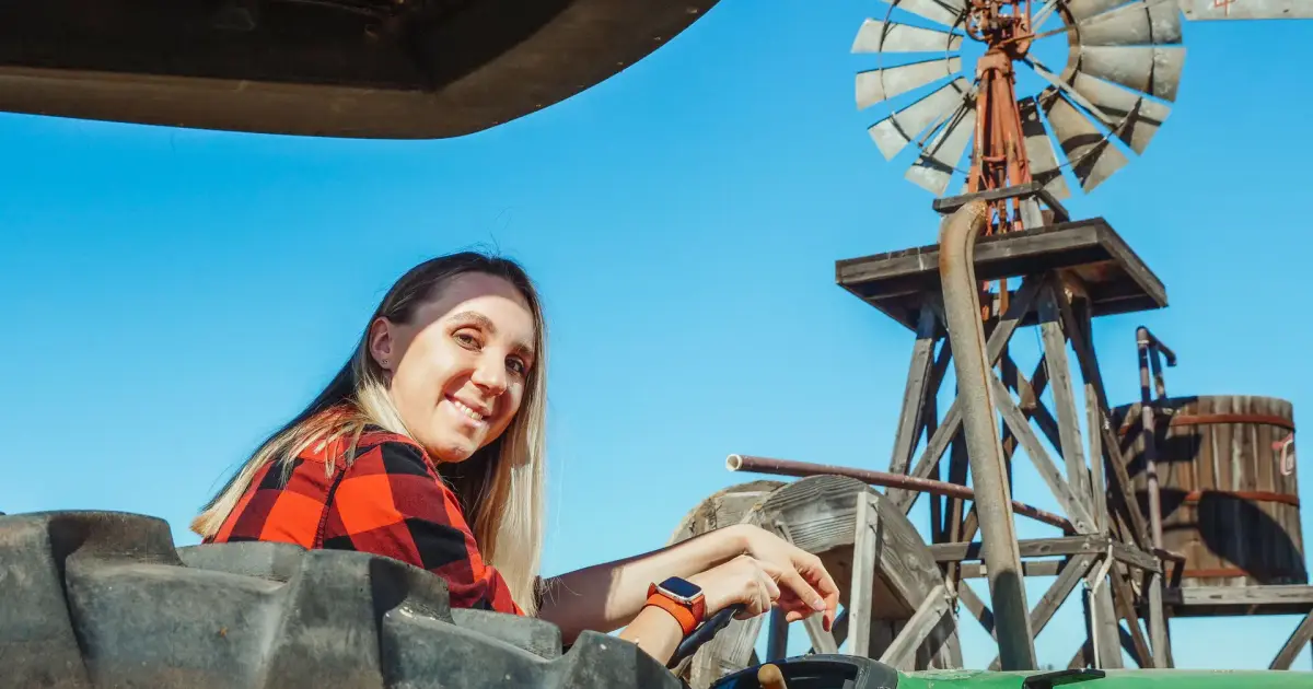 Jovem sorrindo ao volante de um trator numa fazenda