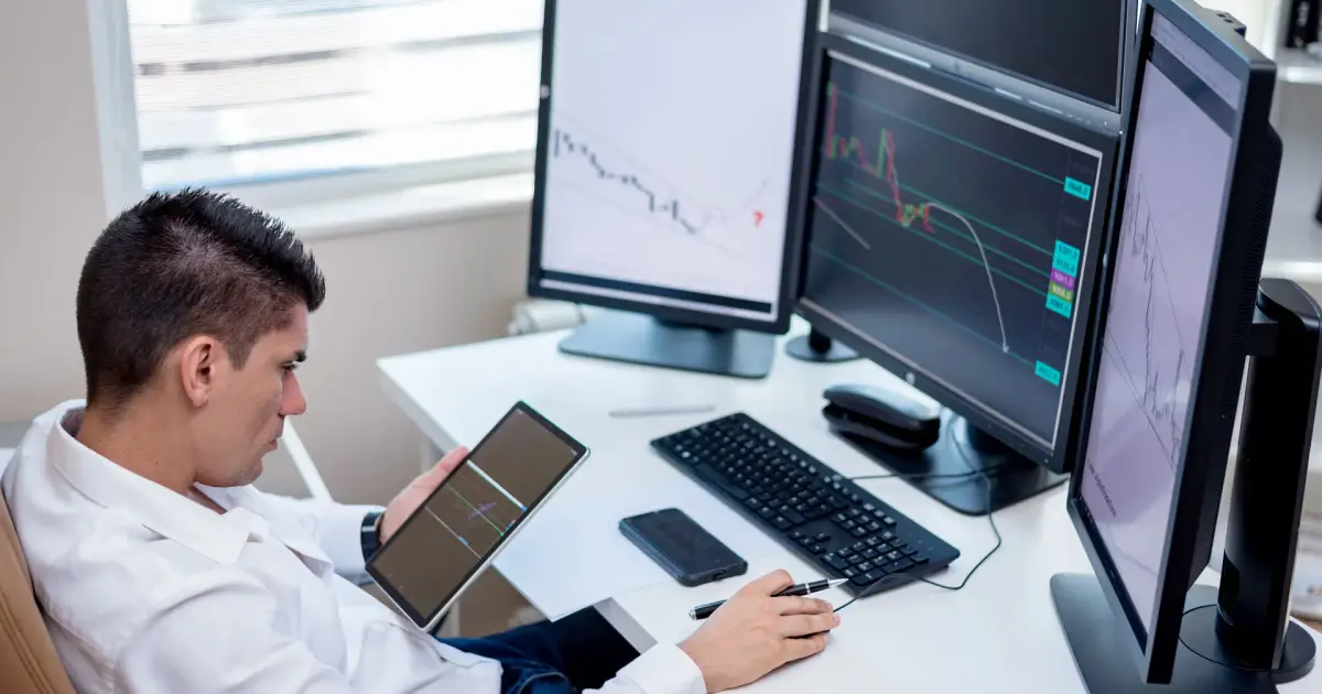 Profissional analisando gráficos de mercado em vários monitores