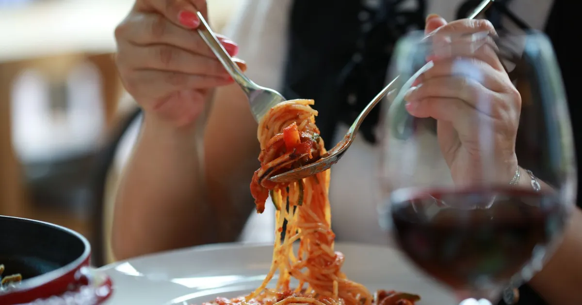 Garfo enrolando espaguete ao molho de tomate ao lado de uma taça de vinho — palavras italianas usadas no inglês, como pasta e al dente