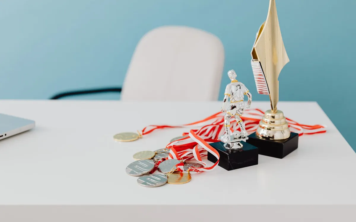 Troféu dourado e medalhas sobre uma mesa de escritório branca, ao lado de um laptop, para o texto em inglês com superlativo sobre a premiação da equipe