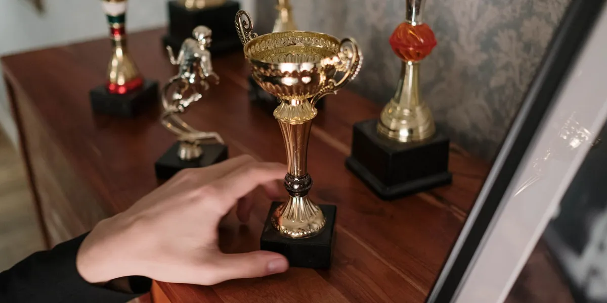 Uma mão alcançando um troféu dourado numa estante de troféus — a cena da história The Trophy