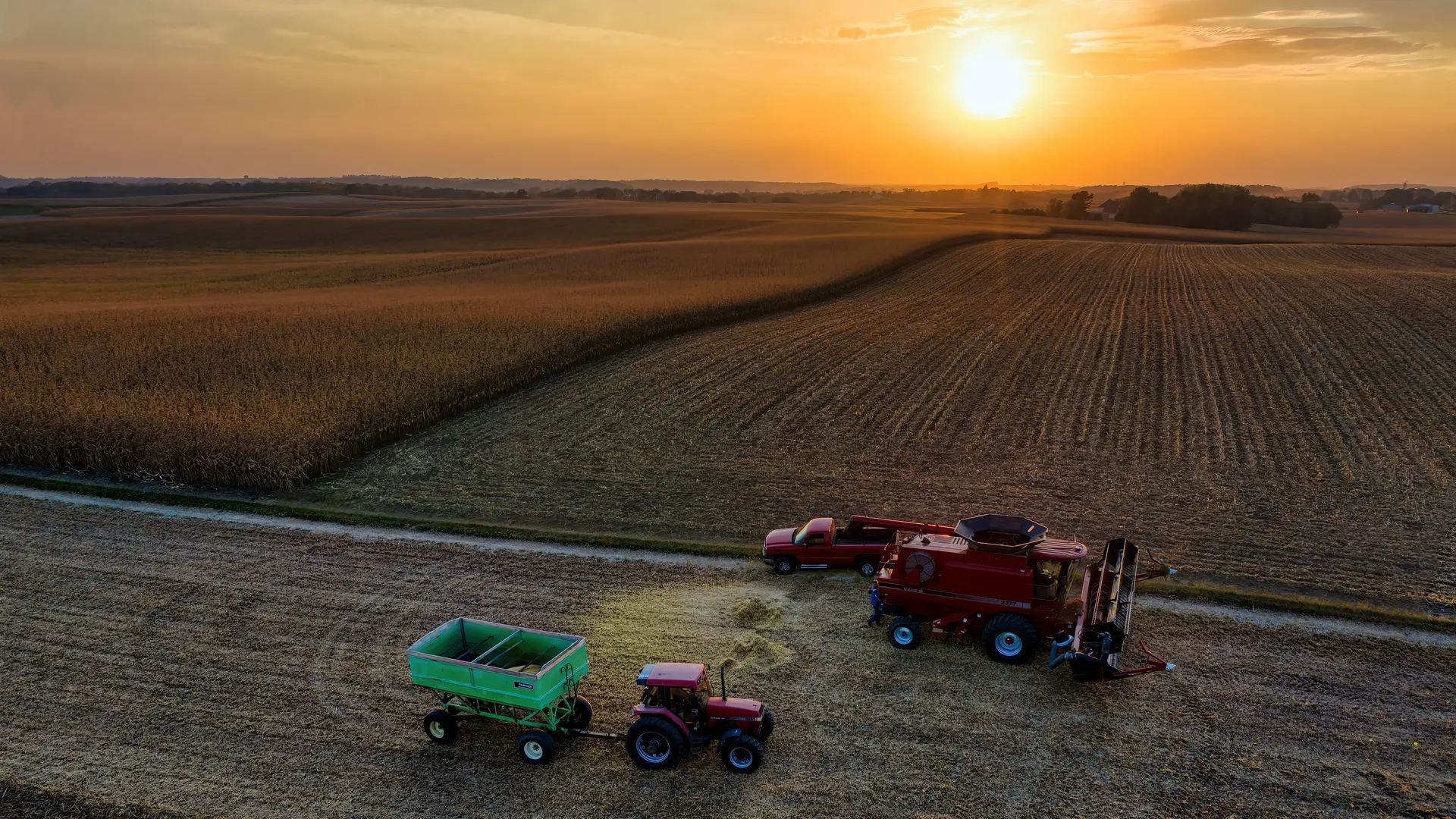 Colheitadeira e tratores na colheita de soja ao pôr do sol, vistos do alto
