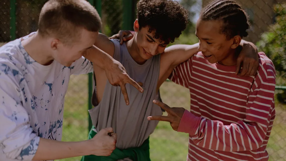 Três amigos adolescentes rindo e brincando juntos ao ar livre
