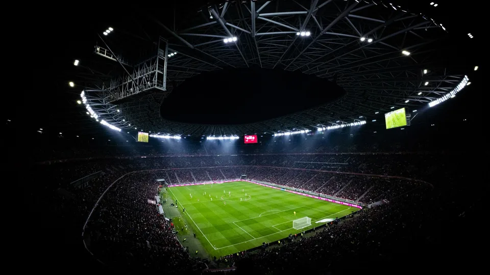 Estádio de futebol lotado à noite, com os refletores acesos
