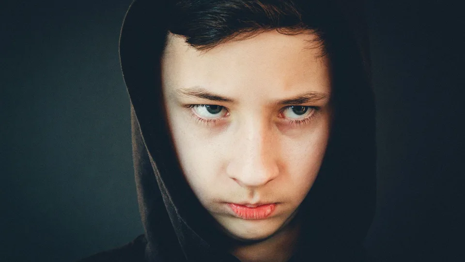 Adolescente de capuz encarando a câmera, sério