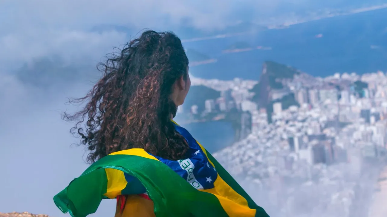 Brasileira de costas, com a bandeira do Brasil nos ombros, olhando o Rio de Janeiro do alto de uma pedra