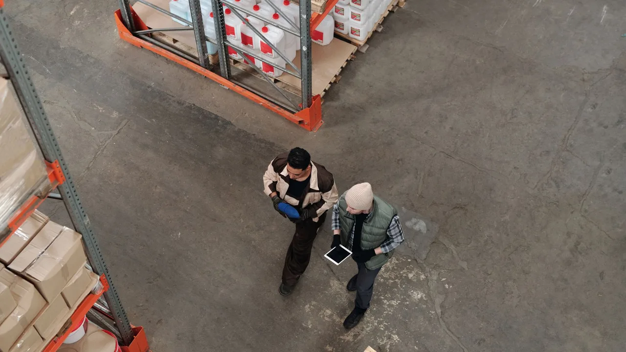 Dois operadores conferindo um tablet no corredor de um armazém logístico