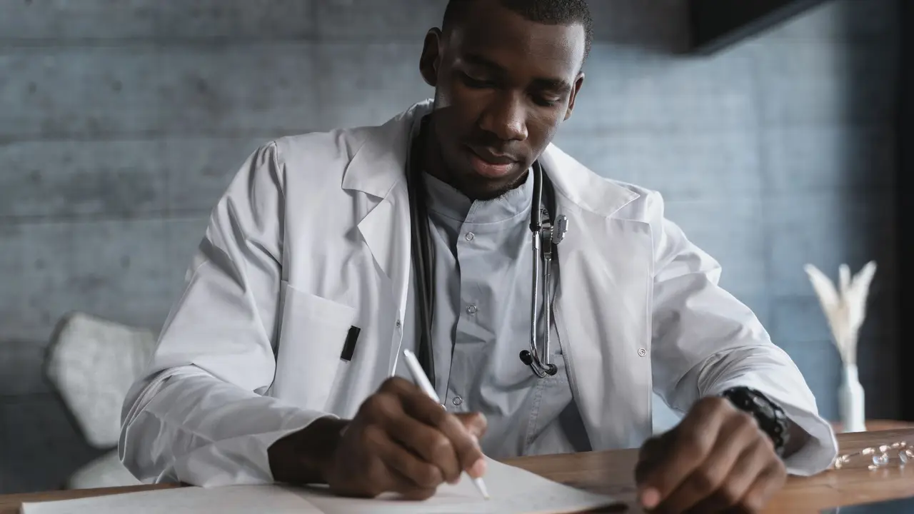 Médico de jaleco escrevendo à mão numa mesa de madeira