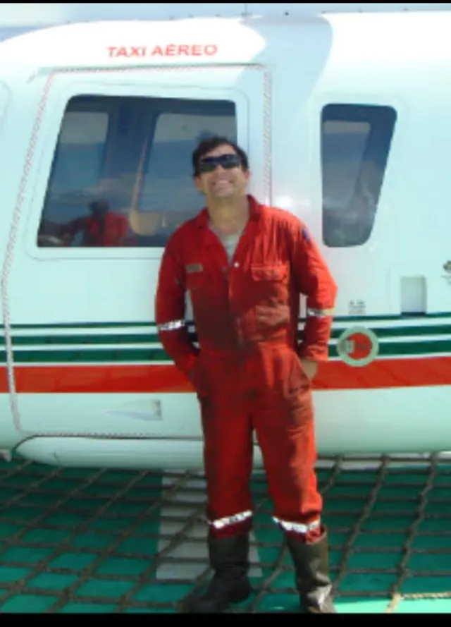 Thiago de macacão laranja em frente a um helicóptero de transporte, na época em que trabalhava na indústria de óleo e gás